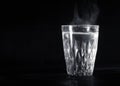 Transparent glass cup with swell the boiling water into it. The vapor from the top. Black background. Royalty Free Stock Photo