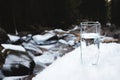 A transparent glass glass with drinking mountain water stands in the snow against a background of a clean mountain river