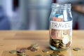 Transparent glass jar labeled travel with euro money in it and outside on top of the wooden table. Background out of focus. Bokeh. Royalty Free Stock Photo