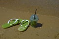 a glass of lemonade with a straw and summer flip-flops on the seashore, sunny beach, summer vacation. background for the design. Royalty Free Stock Photo