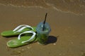 a glass of lemonade with a straw and summer flip-flops on the seashore, sunny beach, summer vacation. background for the design. Royalty Free Stock Photo