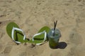 a glass of lemonade with a straw and summer flip-flops on the seashore, sunny beach, summer vacation. background for the design. Royalty Free Stock Photo