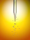 Transparent glass pipette with a Golden liquid dripping