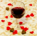 Transparent glass with red wine, heart chocolate and textile red valentine hearts, old paper background, close up