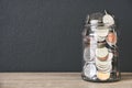 Transparent glass savings jar filled with coins on wooden table with black color wall background, copy space Royalty Free Stock Photo