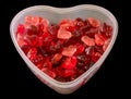 Transparent heart shape vase (bowl) filled with colored (red) heart shape jellies, black background, close up. Royalty Free Stock Photo