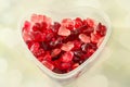 Transparent heart shape vase (bowl) filled with colored (red) heart shape jellies, light hearts background, close up. Royalty Free Stock Photo