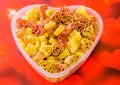 Transparent heart shape vase (bowl) filled with colored (red, yellow an orange) heart shape pasta, colored degradee background Royalty Free Stock Photo