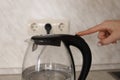Transparent kettle with a black handle girl presses the button on the inclusion button with her finger