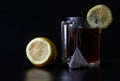 A transparent mug with black tea and a triangular pyramid tea bag stands on a black background next to a cut fresh lemon. Concept Royalty Free Stock Photo