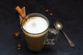 Transparent mug of Cappuccino or latte, scattered coffee beans, spoon, cinnamon sticks, anise star on black background