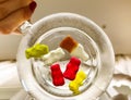 Transparent mug, round and large, filled with water. at the bottom of the mug are gummy bears and bottles of lemonade. girl