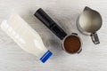 Transparent plastic bottle with milk, portafilter with ground coffee, pitcher on wooden table. Top view