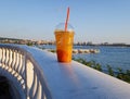 a transparent plastic glass with a cocktail stands on a white fence on the embankment against Royalty Free Stock Photo