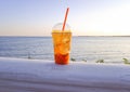 a transparent plastic glass with a cocktail stands on a white fence on the embankment against Royalty Free Stock Photo