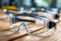 Transparent protective eyewear with black frames resting on a wooden surface in a bright indoor workshop environment focused on Royalty Free Stock Photo