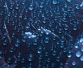 Transparent raindrops flow down on the glass  surface of a deep blue background and are lit by the rays of the bright sun Royalty Free Stock Photo