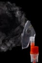 Transparent respiratory mask on atomizing cup with steam on black background