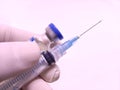 Transparent syringe with closed cap and a vaccine vial hold by doctor's hand in rubber glove