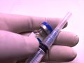 Transparent syringe with closed cap and a vaccine vial hold by doctor's hand in rubber glove