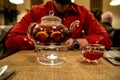 A transparent teapot with fruit tea stands on a table in a cafe in front of a defocused man in a red shirt Royalty Free Stock Photo