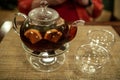 A transparent teapot with fruit tea stands on a table in a cafe in front of a defocused man in a red shirt Royalty Free Stock Photo