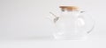 A transparent teapot made of tempered glass with a wooden lid and a metal spiral strainer on a white background. Element of modern