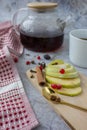 A transparent teapot with strong black tea, a red napkin, apple slices, berries and spices lie on the table Royalty Free Stock Photo