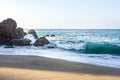 Transparent tourqouise blue wave tube breaking with foam on shoreline with large boulders Royalty Free Stock Photo