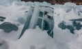 A transparent turquoise ice floe on a frozen lake is surrounded by snow.