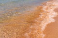 Transparent waves of pure sea waves with foam roll on a golden sandy deserted beach on a sunny day Royalty Free Stock Photo