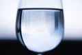 Transparent wine glass with water in the middle, small bubbles. Blue black white blurred background Royalty Free Stock Photo