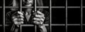 Trapped woman prisoner behind iron bars. Sad adult girl holding a steel cage. Black and white photography. Close-up of