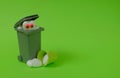 A trash can, a white heart with eyes looking at a broken heart at the bottom and a small green bucket on a bright green background Royalty Free Stock Photo