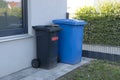 Trash cans of black and blue on wheels stand near the wall. Dirty mobile trash bins and household waste. Sorting garbage into Royalty Free Stock Photo