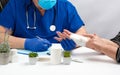 Traumatologist doctor in blue latex medical gloves sits at a table and holds a patient reception with a hand injury