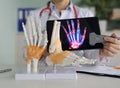 A traumatologist examines a model of a skeleton of an arm and leg while displaying a digital image of the anatomy of the
