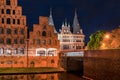 Trave shore at night with salt storage and Holstentor in background in Lubeck, Germany