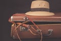 Travel and adventure concept. Vintage brown suitcase with fedora hat and bullwhip on dark