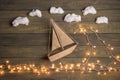 Travel and adventure creative concept - toy boat on a wooden background with cotton clouds. Christmas lights as a sea waves