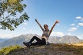 Travel, adventure and trekking by Hiking in the mountains. girl is sitting on a scenic peak, her hands spread out in the air