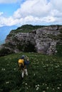 Male tourist with yellow large backpack travels together alone on plateau and studies new beauty of alpine meadows. Travel alone