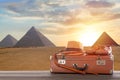 Travel, archeology and adventure concept. Vintage brown suitcase with fedora hat, bullwhip and shoes against Great pyramids in