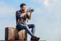 Travel blog. Man sit on suitcase. Handsome guy traveler retro camera. Guy outdoors with vintage suitcase
