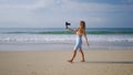 Influencer in white outfit records beach vlog with pro camera, wireless lav mic. Travel blogger captures ocean views