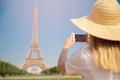 Travel blogger young woman in hat takes photograph of Eiffel Tower on telephone in Paris, France Royalty Free Stock Photo