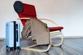 Travel blue suitecase stands near red armchair with coat and picky blinders hat