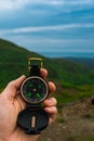 Travel, camping, orienteering and navigation concept - black magnetic compass close-up in a man s hand, blurred landscape