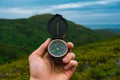 Travel, camping, orienteering and navigation concept - black magnetic compass close-up in a man s hand, blurred landscape