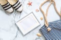 Travel composition on a marble background. Women`s desk with striped sandals, beach bag, seashells and blank picture frame. Lifes